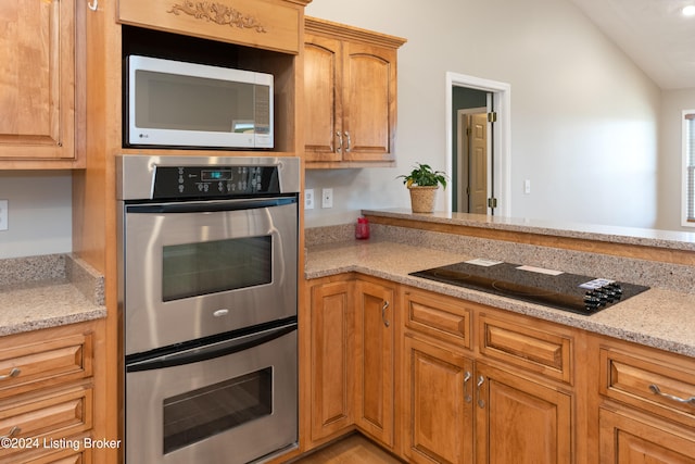 kitchen with black electric cooktop, lofted ceiling, light stone countertops, and double oven