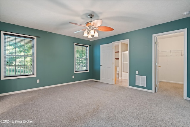 unfurnished bedroom featuring ceiling fan, multiple windows, carpet flooring, and a walk in closet