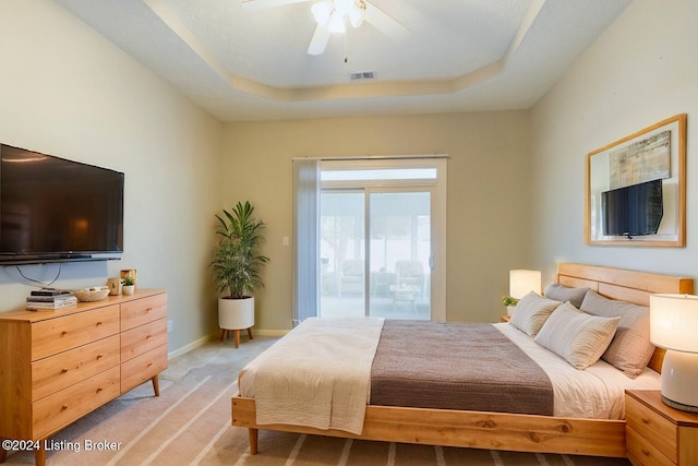 bedroom with access to exterior, light colored carpet, ceiling fan, and a tray ceiling