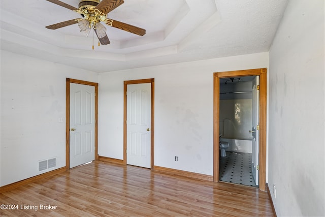 unfurnished bedroom featuring ensuite bathroom, a tray ceiling, ceiling fan, and light hardwood / wood-style flooring