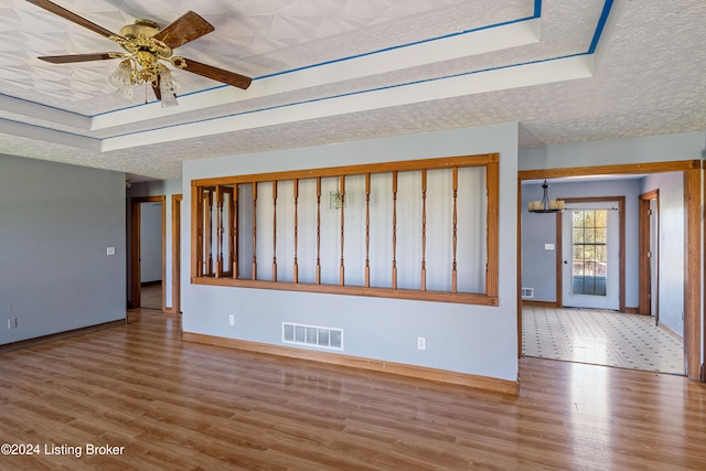 unfurnished room with light hardwood / wood-style floors, ceiling fan, a textured ceiling, and a raised ceiling