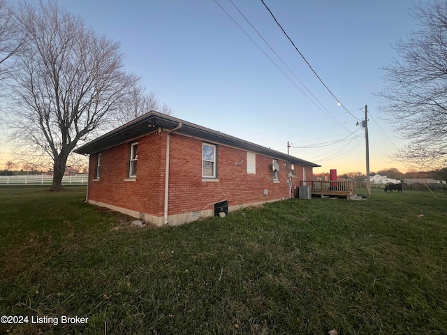 property exterior at dusk with a deck, central AC unit, and a yard