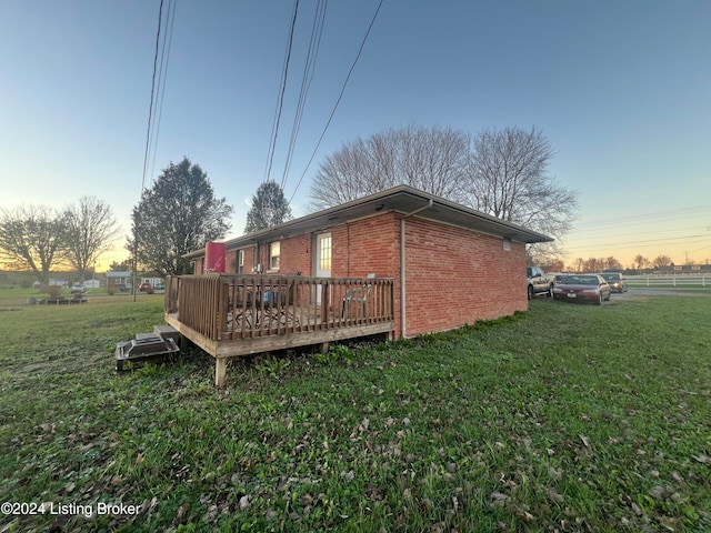 property exterior at dusk featuring a yard and a deck