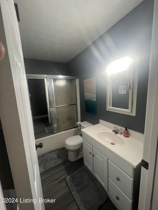 full bathroom featuring a textured ceiling, shower / bath combination with glass door, wood-type flooring, vanity, and toilet