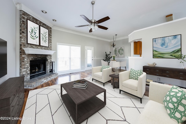 living room featuring a brick fireplace, ceiling fan, light hardwood / wood-style floors, and ornamental molding