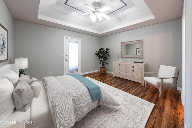 bedroom with a tray ceiling, crown molding, ceiling fan, and dark wood-type flooring