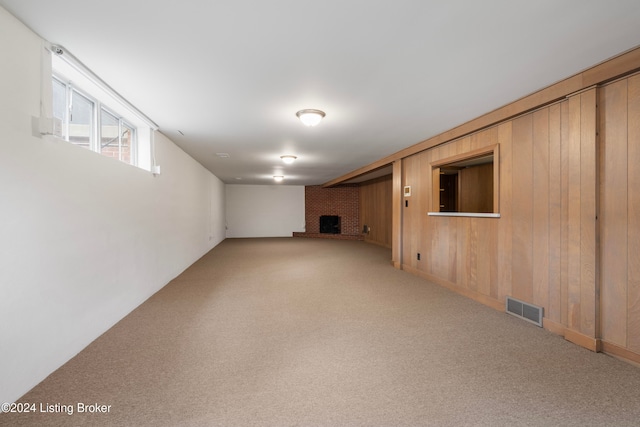 basement featuring carpet, wood walls, and a brick fireplace