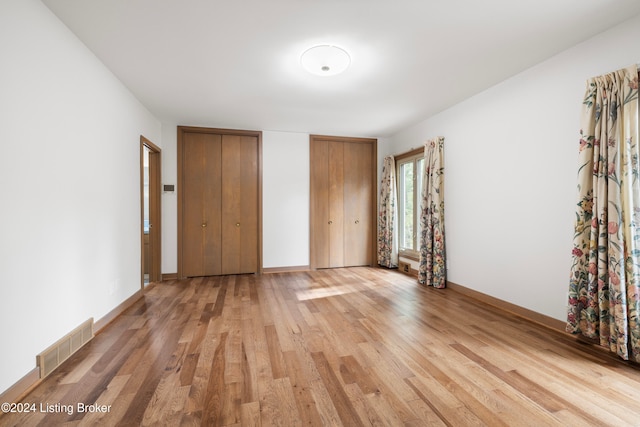 unfurnished bedroom featuring light wood-type flooring and two closets