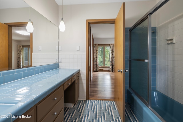 bathroom featuring hardwood / wood-style flooring, vanity, shower / bath combination with glass door, and tile walls