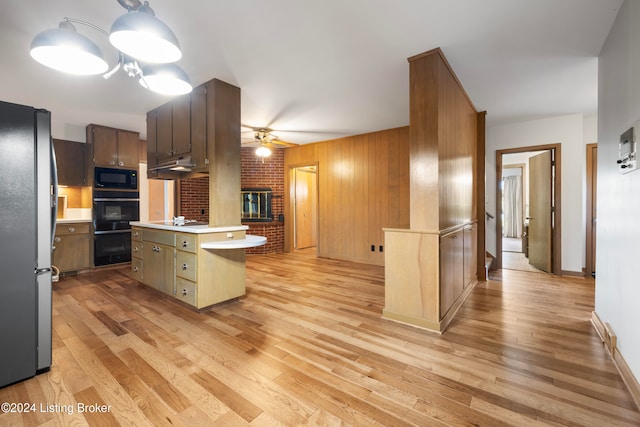 kitchen featuring ceiling fan, wood walls, light hardwood / wood-style floors, a kitchen island with sink, and black appliances