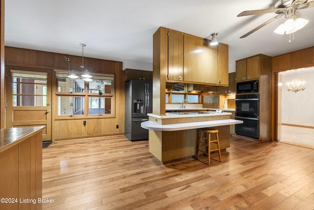 kitchen with a kitchen breakfast bar, decorative light fixtures, wooden walls, black appliances, and light wood-type flooring