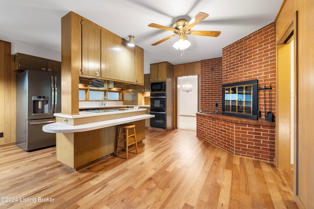 kitchen with ceiling fan, kitchen peninsula, light hardwood / wood-style floors, a kitchen bar, and black appliances