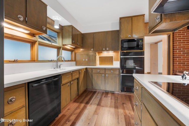 kitchen featuring brick wall, sink, black appliances, light hardwood / wood-style flooring, and range hood