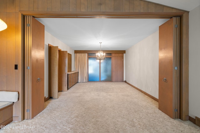 carpeted empty room featuring an inviting chandelier, lofted ceiling, and wood walls