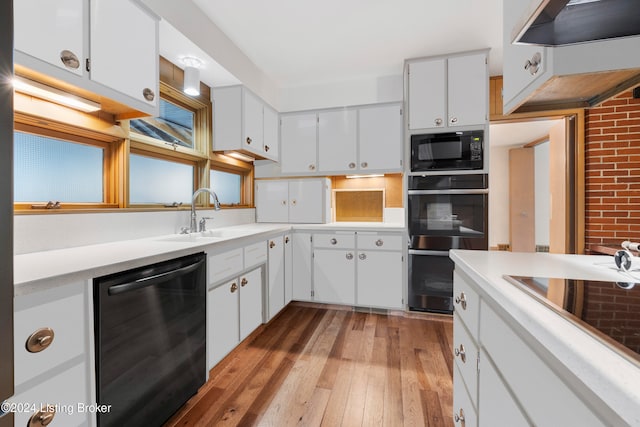 kitchen featuring white cabinetry, black appliances, brick wall, and light hardwood / wood-style floors