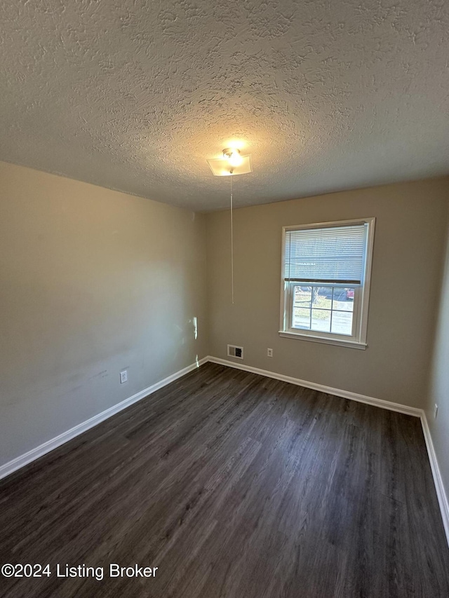 empty room with dark wood-type flooring and a textured ceiling