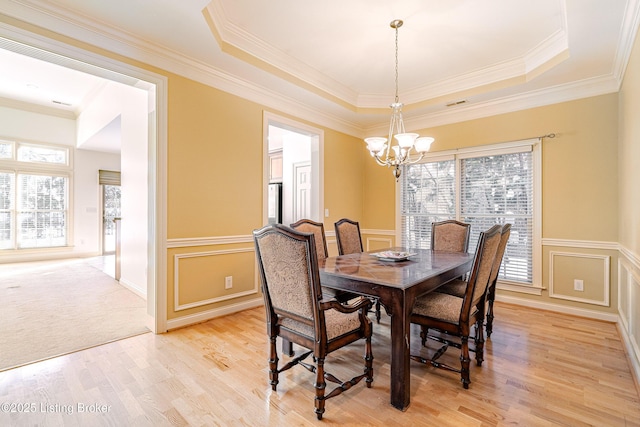 dining space featuring a raised ceiling, an inviting chandelier, and light hardwood / wood-style floors