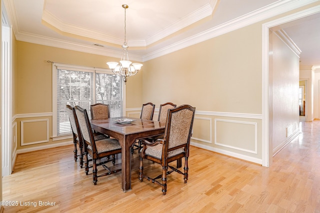 dining room with a tray ceiling, light wood-type flooring, ornamental molding, and a notable chandelier