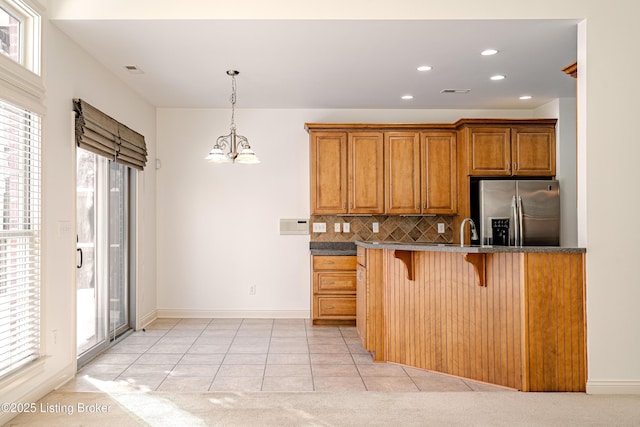 kitchen featuring light tile patterned flooring, a breakfast bar area, hanging light fixtures, stainless steel refrigerator with ice dispenser, and tasteful backsplash