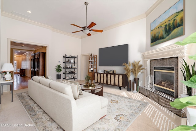 living room with ornamental molding, ceiling fan, light colored carpet, and a tiled fireplace