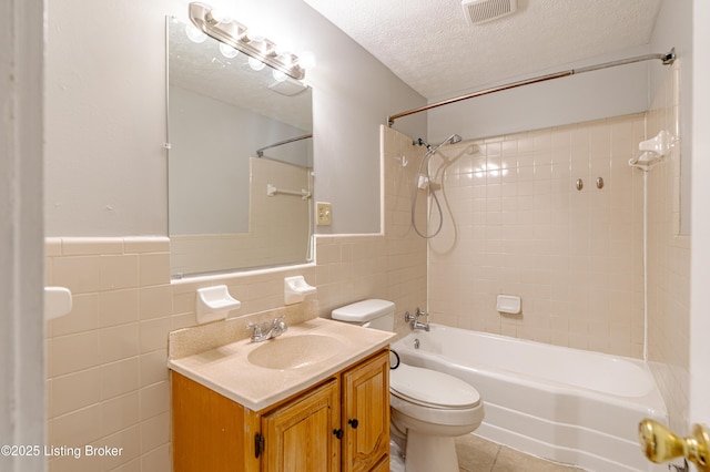 full bathroom with toilet, a textured ceiling, tile walls, vanity, and tiled shower / bath combo