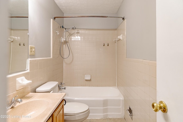 full bathroom with tiled shower / bath, tile walls, vanity, toilet, and a textured ceiling