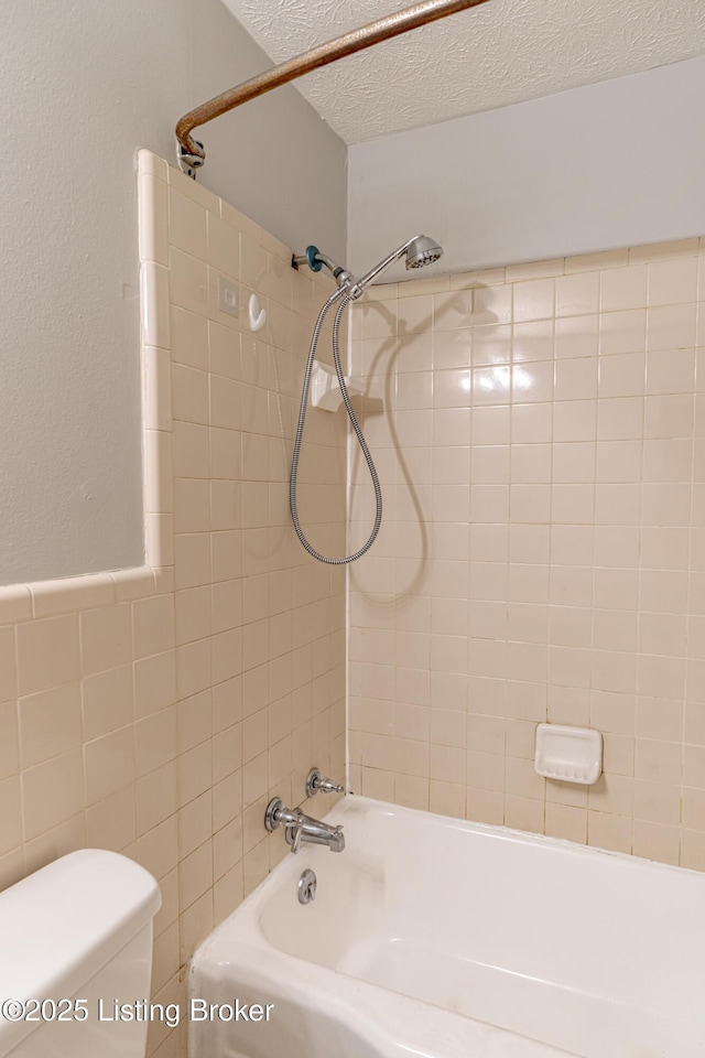 bathroom with tile walls, tiled shower / bath, toilet, and a textured ceiling