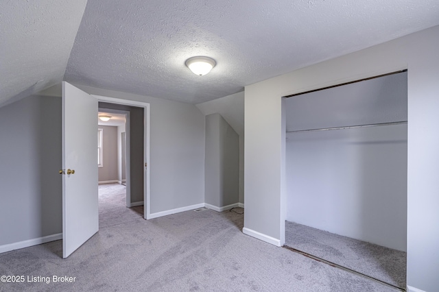 unfurnished bedroom with vaulted ceiling, light carpet, a textured ceiling, and a closet