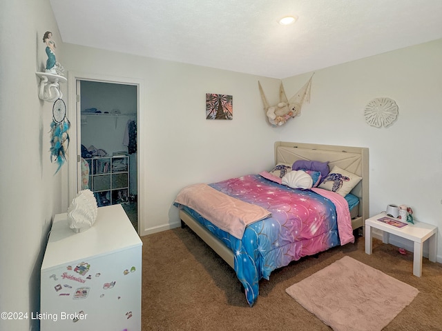 bedroom featuring a walk in closet, a closet, refrigerator, and dark colored carpet