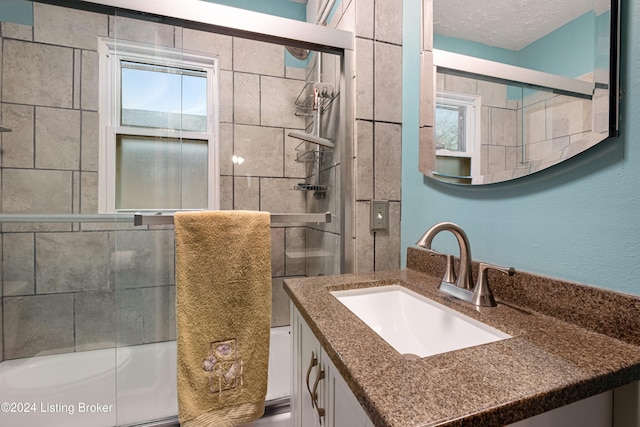 bathroom featuring shower / bath combination with glass door, a textured ceiling, a healthy amount of sunlight, and vanity