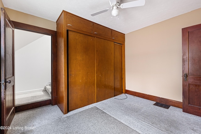 unfurnished bedroom featuring a textured ceiling, ceiling fan, a closet, and light carpet