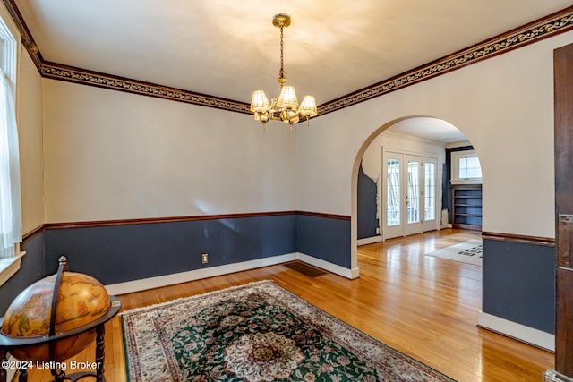 interior space featuring a chandelier, french doors, light wood-type flooring, and crown molding