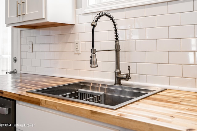 room details featuring decorative backsplash, sink, dishwasher, white cabinets, and butcher block counters