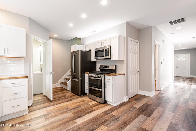 kitchen with appliances with stainless steel finishes, tasteful backsplash, light hardwood / wood-style floors, white cabinets, and butcher block countertops