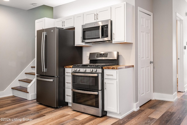 kitchen with butcher block countertops, white cabinetry, hardwood / wood-style floors, and stainless steel appliances