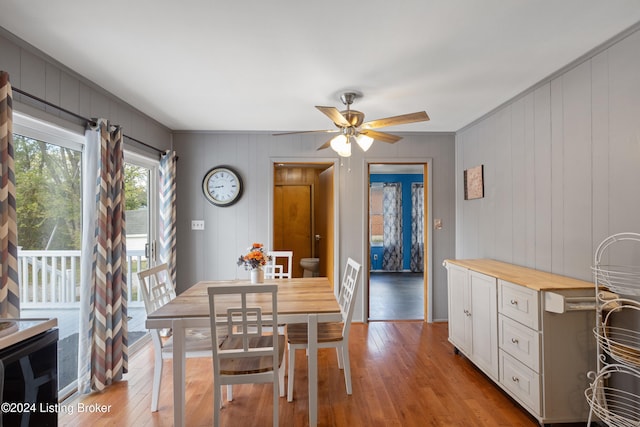 dining space featuring ceiling fan, light hardwood / wood-style floors, ornamental molding, and wooden walls