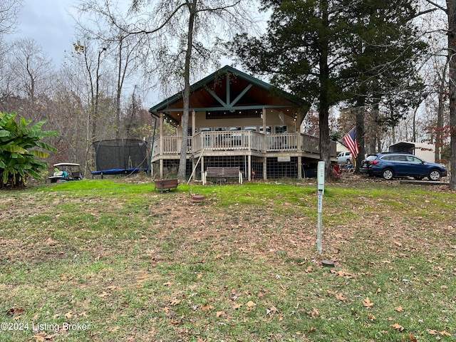 back of property featuring a trampoline, a deck, and a lawn