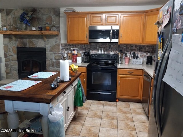 kitchen featuring decorative backsplash, a stone fireplace, black appliances, and light tile patterned floors