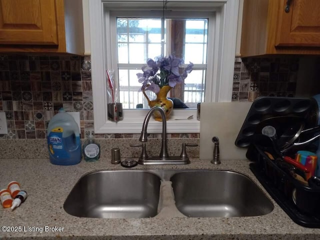 kitchen featuring light stone counters, backsplash, and a sink