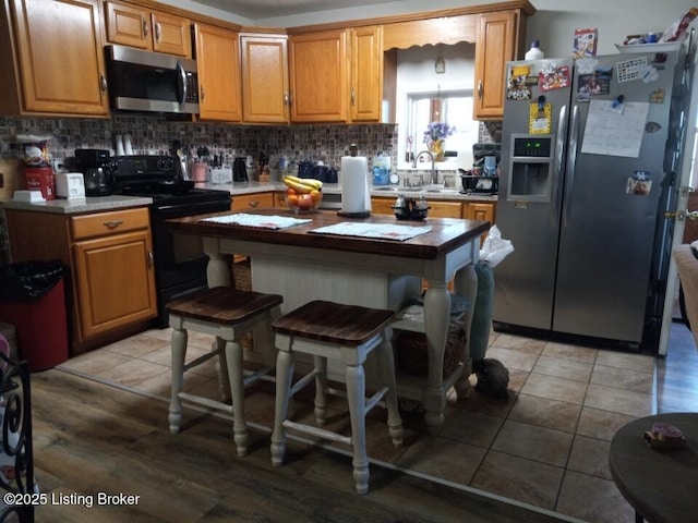 kitchen with light tile patterned floors, brown cabinets, a sink, stainless steel appliances, and backsplash