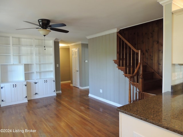 unfurnished living room with dark hardwood / wood-style flooring, ceiling fan, ornamental molding, and wood walls