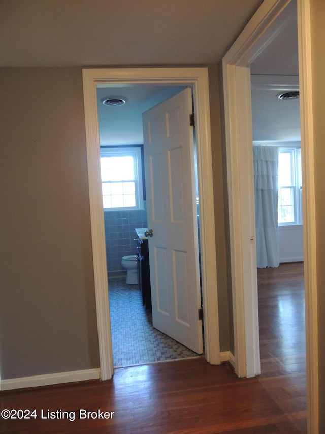 corridor with dark hardwood / wood-style flooring, plenty of natural light, and tile walls