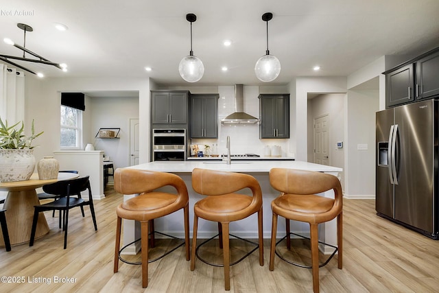 kitchen with stainless steel appliances, an island with sink, a breakfast bar area, and wall chimney exhaust hood