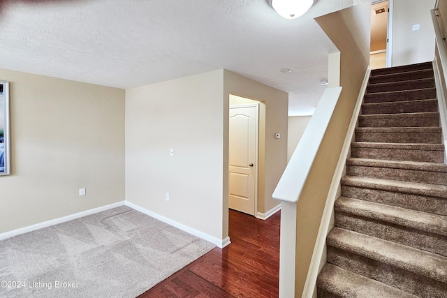 stairway with wood-type flooring and a textured ceiling