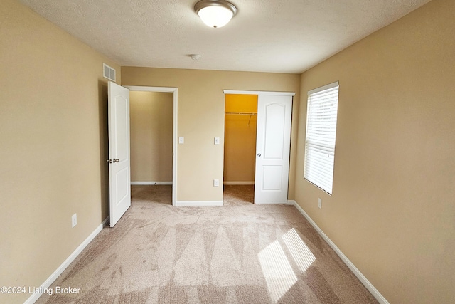 unfurnished bedroom featuring light colored carpet, a spacious closet, a textured ceiling, and a closet