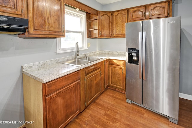 kitchen with light wood-type flooring, stainless steel fridge with ice dispenser, sink, and exhaust hood