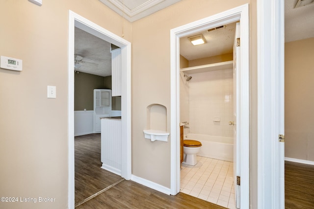 bathroom with ceiling fan, tiled shower / bath combo, toilet, a textured ceiling, and wood-type flooring