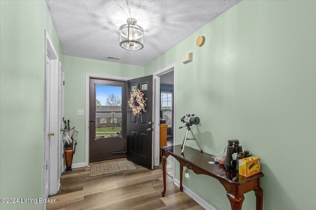 foyer with a textured ceiling, light wood-type flooring, and a notable chandelier