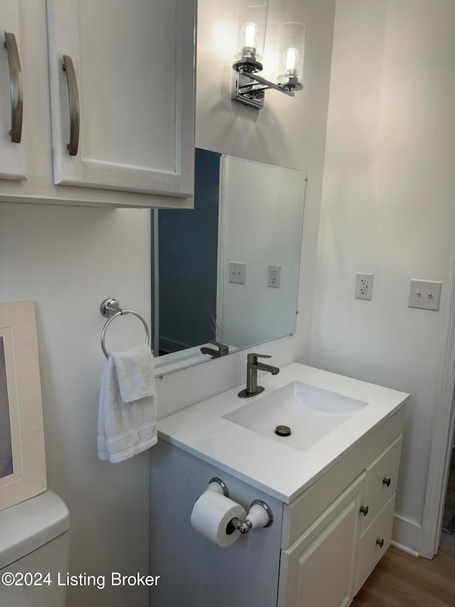 half bath with toilet, wood finished floors, and vanity