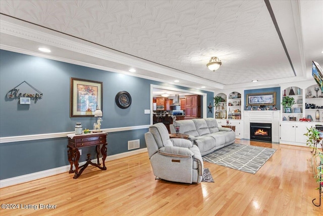 living room with hardwood / wood-style floors, built in shelves, and ornamental molding